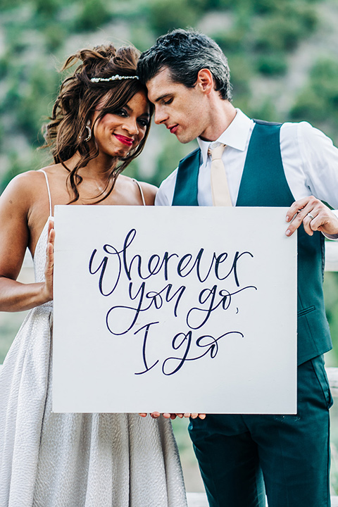  a greenery las vegas wedding at a rustic venue with the bride in an A-line gown and the groom in a green suit – couple with wedding sign
