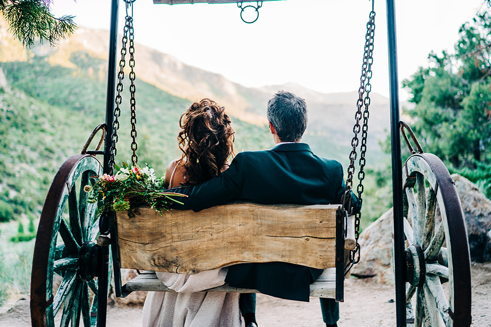  a greenery las vegas wedding at a rustic venue with the bride in an A-line gown and the groom in a green suit – couple sitting in the swing