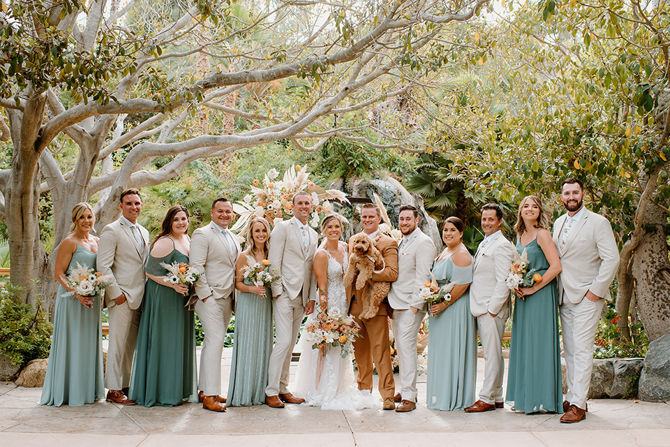  earth-toned boho wedding with the bridesmaids in green dresses, groomsmen in tan suits, and the groom in a caramel suit – bridal party