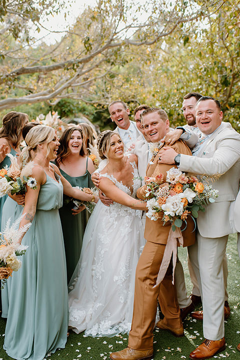  earth-toned boho wedding with the bridesmaids in green dresses, groomsmen in tan suits, and the groom in a caramel suit – bridalparty