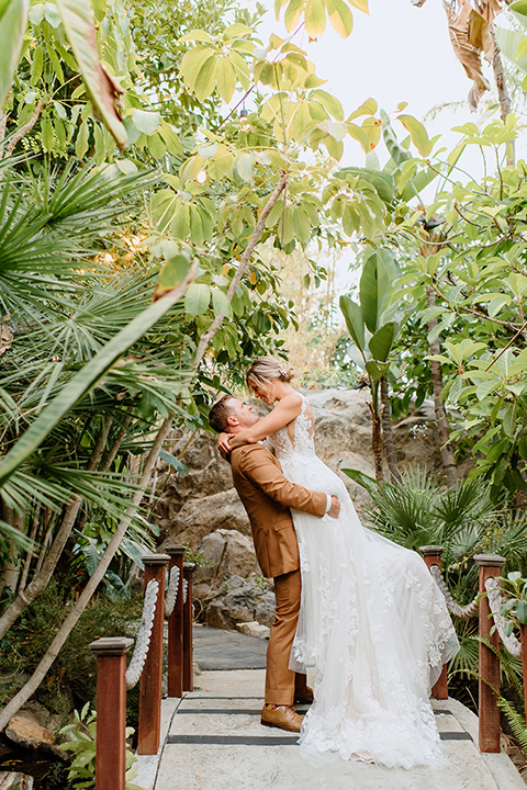  earth-toned boho wedding with the bridesmaids in green dresses, groomsmen in tan suits, and the groom in a caramel suit – couple kissing
