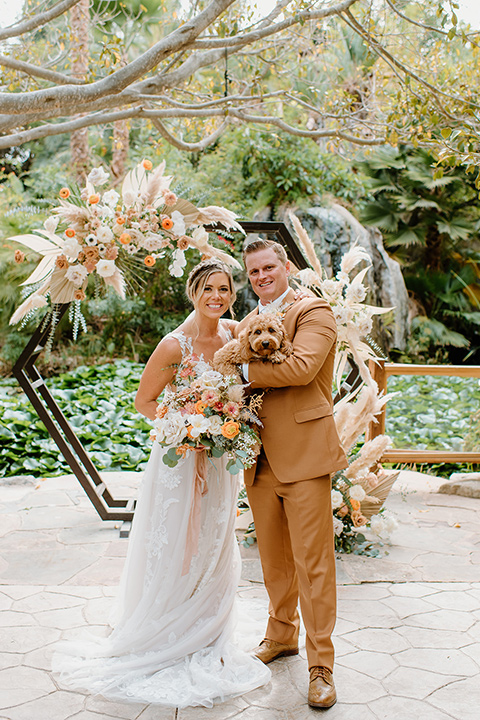  earth-toned boho wedding with the bridesmaids in green dresses, groomsmen in tan suits, and the groom in a caramel suit – couple with their dog