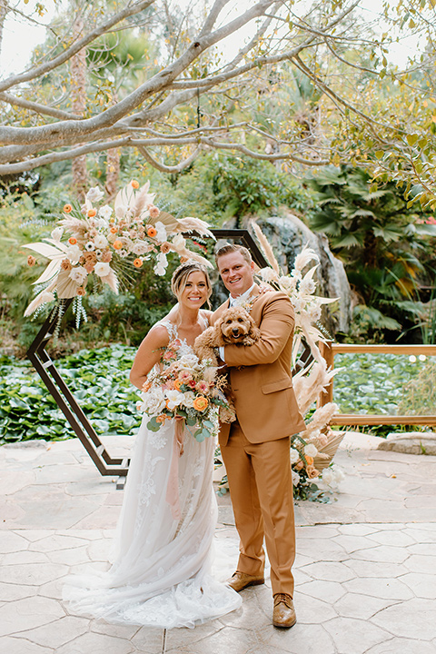  earth-toned boho wedding with the bridesmaids in green dresses, groomsmen in tan suits, and the groom in a caramel suit – couple with their dog 