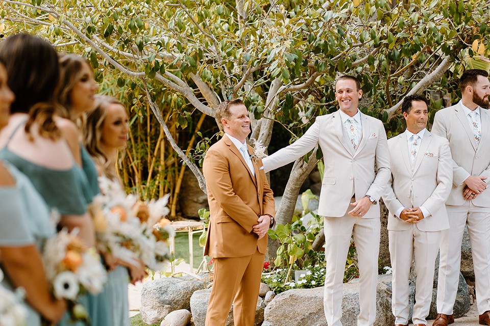  earth-toned boho wedding with the bridesmaids in green dresses, groomsmen in tan suits, and the groom in a caramel suit – groom at ceremony