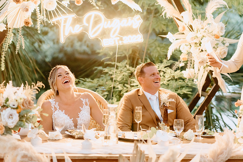  earth-toned boho wedding with the bridesmaids in green dresses, groomsmen in tan suits, and the groom in a caramel suit – couple at sweetheart table