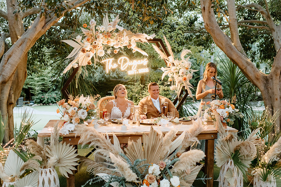  earth-toned boho wedding with the bridesmaids in green dresses, groomsmen in tan suits, and the groom in a caramel suit – sweetheart table and couple