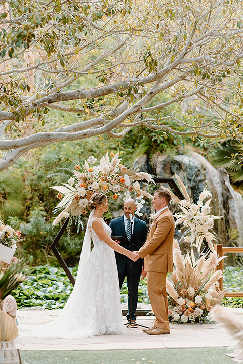  earth-toned boho wedding with the bridesmaids in green dresses, groomsmen in tan suits, and the groom in a caramel suit – couple and their vows