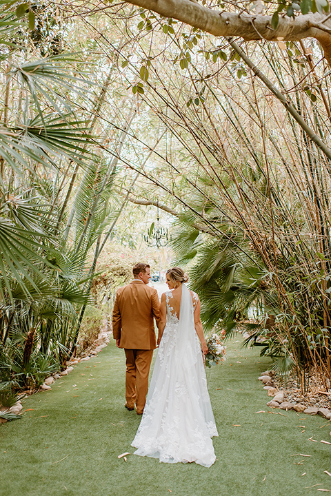 earth-toned boho wedding with the bridesmaids in green dresses, groomsmen in tan suits, and the groom in a caramel suit – couple walking 