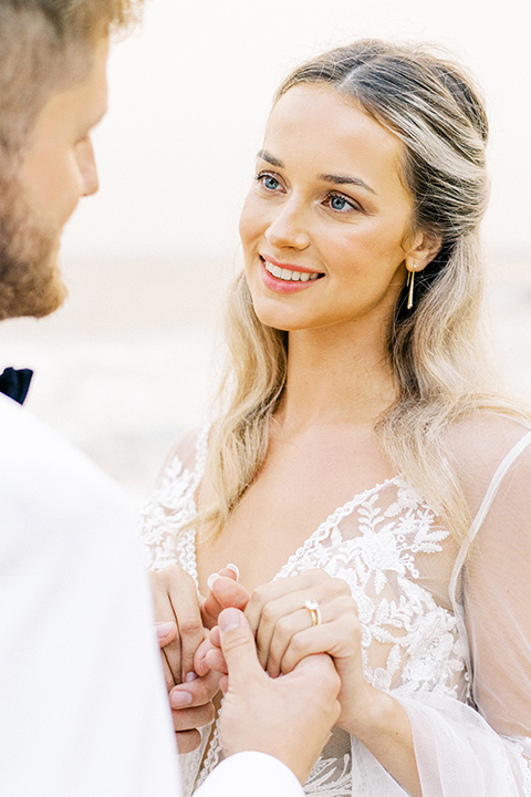  beach side wedding with the bride in a flowing lace gown and the groom in a white tuxedo – couple holding hands