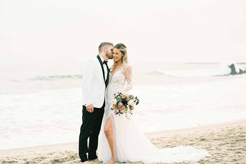  beach side wedding with the bride in a flowing lace gown and the groom in a white tuxedo – kissing