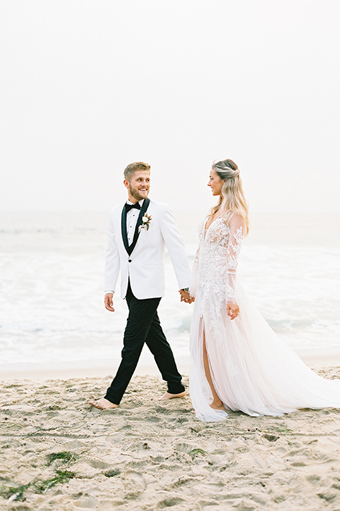  beach side wedding with the bride in a flowing lace gown and the groom in a white tuxedo – couple walking 