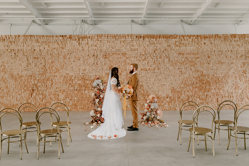  an amber toned wedding in san diego california with the bride in a modern fitted gown with cap sleeves and the groom in a caramel suit – couple at the ceremony 