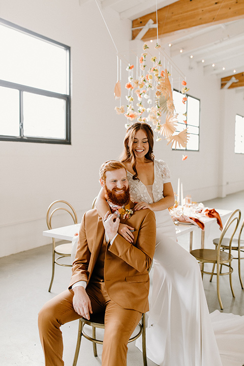  an amber toned wedding in san diego california with the bride in a modern fitted gown with cap sleeves and the groom in a caramel suit – bride and groom sitting at table at the reception 