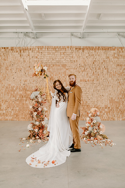  an amber toned wedding in san diego california with the bride in a modern fitted gown with cap sleeves and the groom in a caramel suit – couple at the altar 