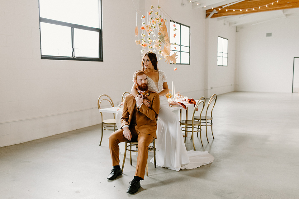  an amber toned wedding in san diego california with the bride in a modern fitted gown with cap sleeves and the groom in a caramel suit – couple sitting at the table at the reception 