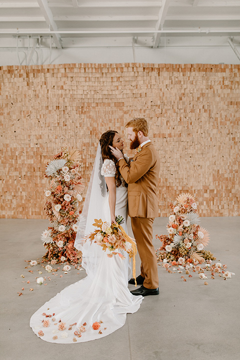  an amber toned wedding in san diego california with the bride in a modern fitted gown with cap sleeves and the groom in a caramel suit – couple at the altar 