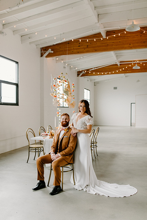  an amber toned wedding in san diego california with the bride in a modern fitted gown with cap sleeves and the groom in a caramel suit – bride and groom sitting at table at the reception 