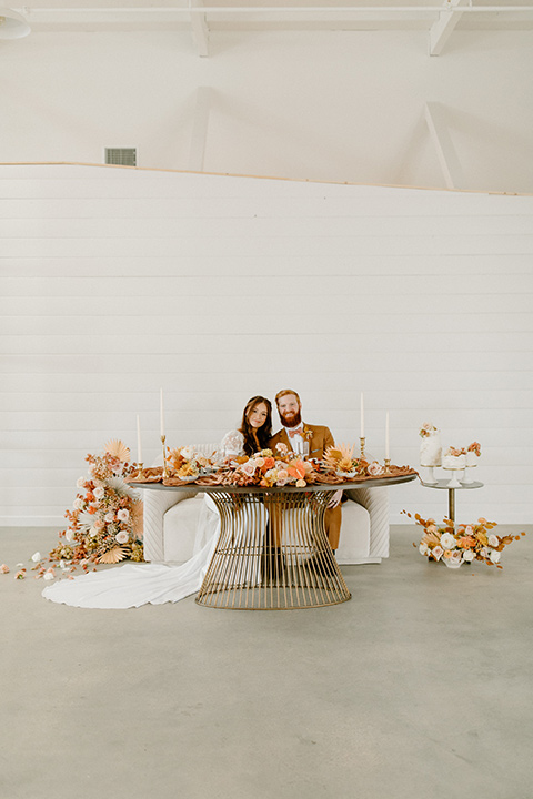  an amber toned wedding in san diego california with the bride in a modern fitted gown with cap sleeves and the groom in a caramel suit – couple at sweetheart table 