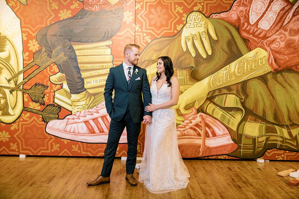  museum of latin american art wedding with 2 different styles – one bride in a fitted gown and the groom in a grey suit and the other bride in a lace gown and the groom in a green suit – couple walking