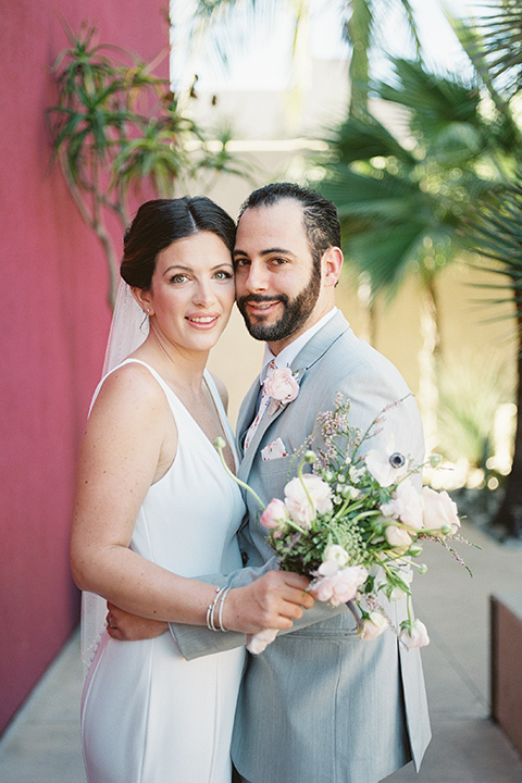  museum of latin american art wedding with 2 different styles – one bride in a fitted gown and the groom in a grey suit and the other bride in a lace gown and the groom in a green suit – couple hugging 