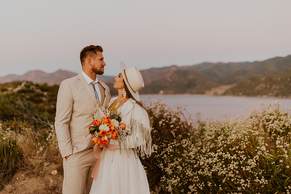  wildflower wedding in a field with the bride in a flowing gown and bridal wings, and the groom in a tan suit and bolo tie – couple looking at the scenery