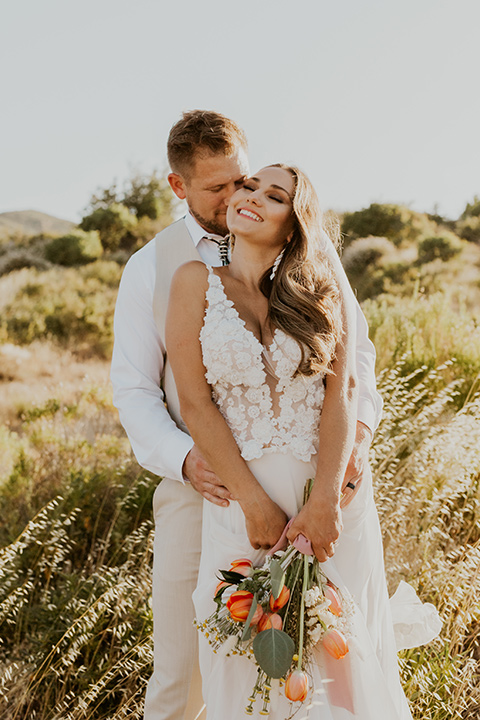  wildflower wedding in a field with the bride in a flowing gown and bridal wings, and the groom in a tan suit and bolo tie - couple embracing 