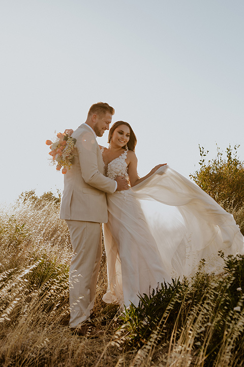  wildflower wedding in a field with the bride in a flowing gown and bridal wings, and the groom in a tan suit and bolo tie - couple embracing 