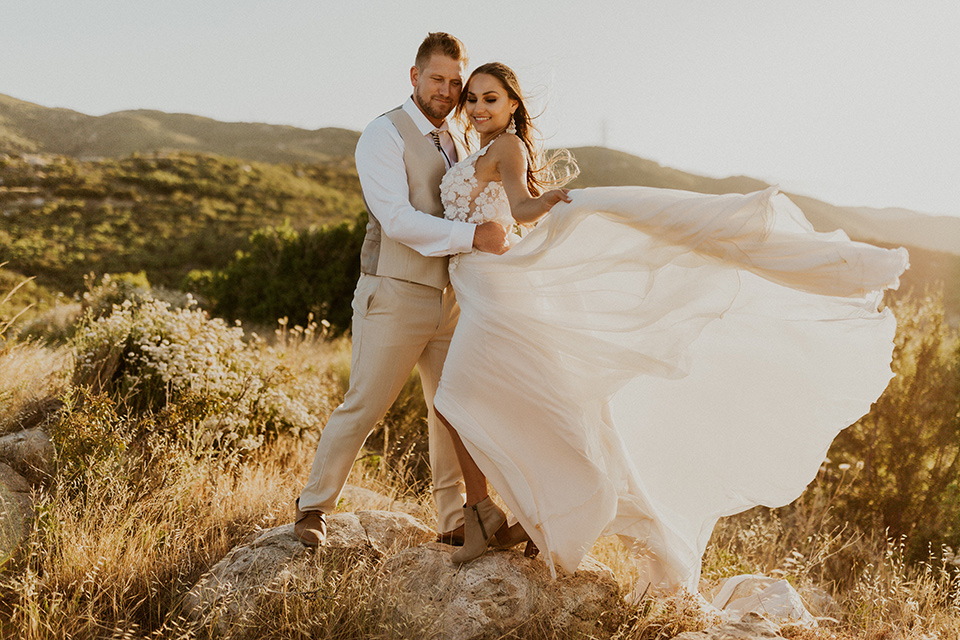  wildflower wedding in a field with the bride in a flowing gown and bridal wings, and the groom in a tan suit and bolo tie – embracing in the wind
