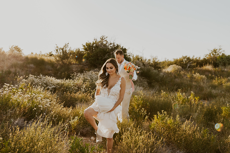  wildflower wedding in a field with the bride in a flowing gown and bridal wings, and the groom in a tan suit and bolo tie – couple walking