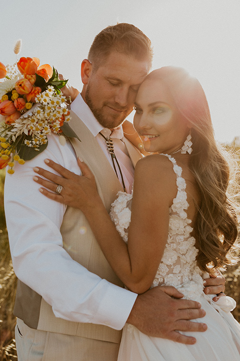  wildflower wedding in a field with the bride in a flowing gown and bridal wings, and the groom in a tan suit and bolo tie – couple embracing