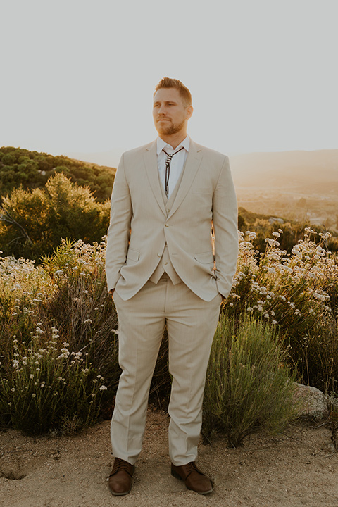  wildflower wedding in a field with the bride in a flowing gown and bridal wings, and the groom in a tan suit and bolo tie – groom