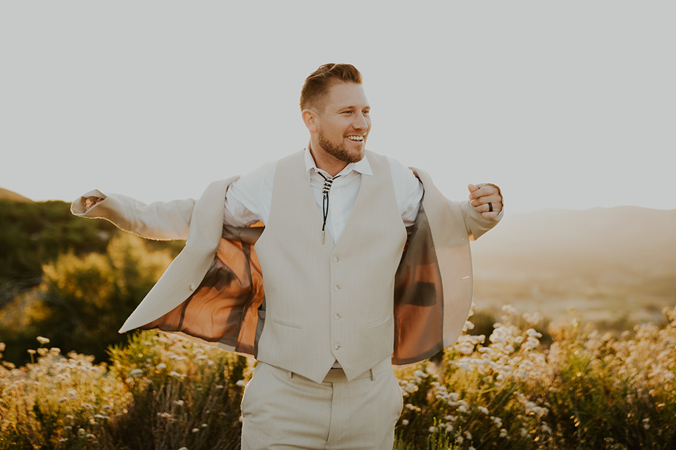  wildflower wedding in a field with the bride in a flowing gown and bridal wings, and the groom in a tan suit and bolo tie – groom