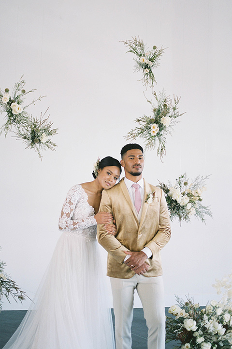  minimalistic nude wedding with vintage touches, the bride in a flowing gown with sleeves and the groom in a tan suit – groom in the gold velvet coat and bride hugging him 