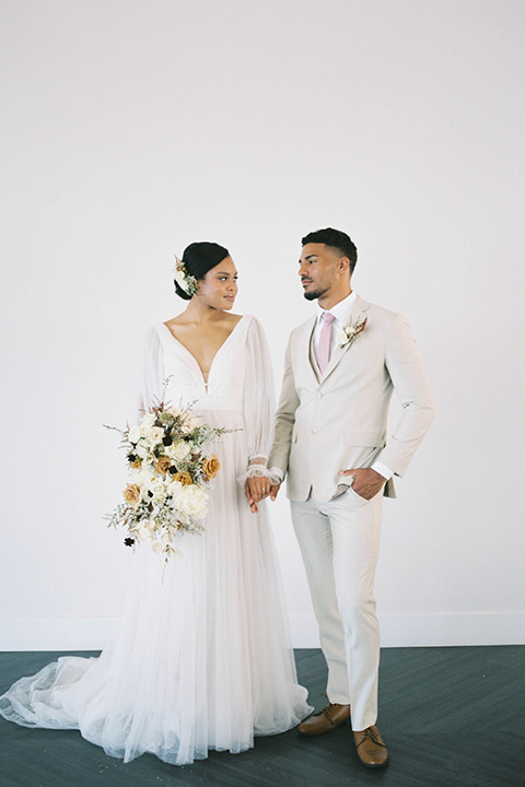  minimalistic nude wedding with vintage touches, the bride in a flowing gown with sleeves and the groom in a tan suit – couple walking 