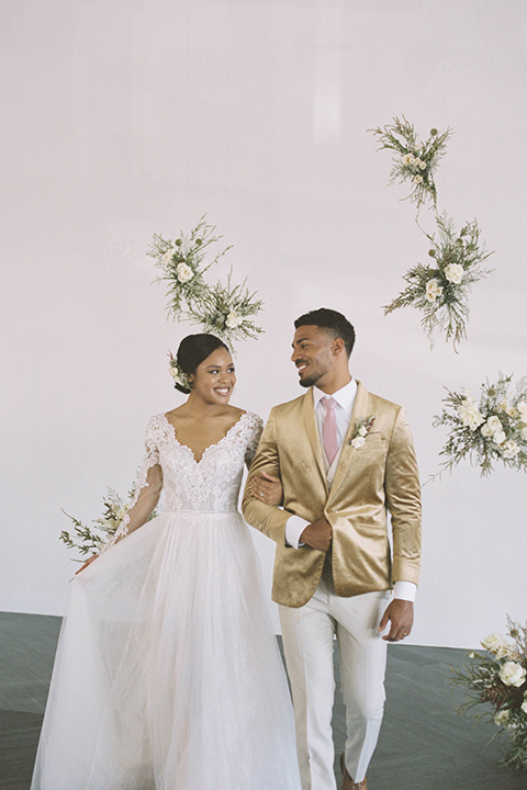  minimalistic nude wedding with vintage touches, the bride in a flowing gown with sleeves and the groom in a tan suit – groom in the gold velvet coat and bride hugging him