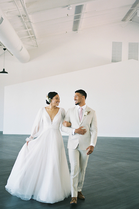  minimalistic nude wedding with vintage touches, the bride in a flowing gown with sleeves and the groom in a tan suit – couple touching walking