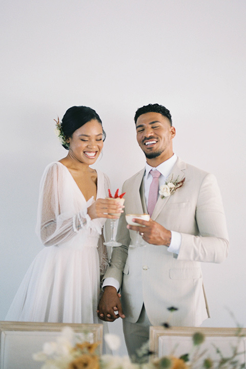  minimalistic nude wedding with vintage touches, the bride in a flowing gown with sleeves and the groom in a tan suit – cheersing 