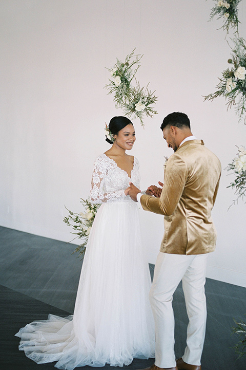  minimalistic nude wedding with vintage touches, the bride in a flowing gown with sleeves and the groom in a tan suit – groom in the gold velvet coat and bride hugging him 