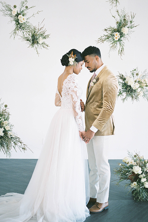  minimalistic nude wedding with vintage touches, the bride in a flowing gown with sleeves and the groom in a tan suit – groom in the gold velvet coat and bride hugging him 