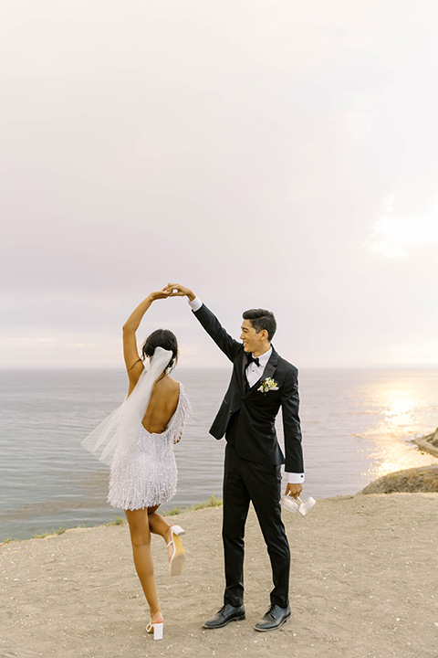  modern black and white upscale wedding on the cliffs overlooking the ocean – bride in short dress and couple on the sand 