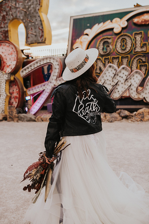  same sex wedding with two brides at the neon museum in las vegas with one brief is a bohemian ballgown and the other in a gold velvet tuxedo coat and tan pants – bride in dress and leather coat