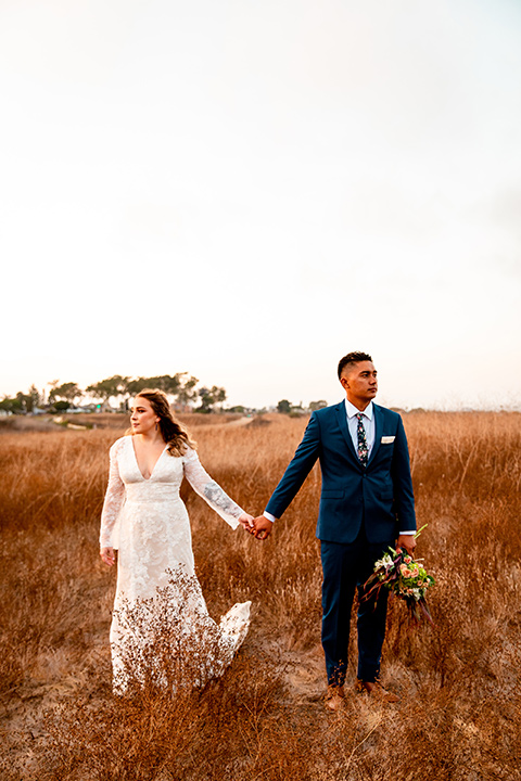  newport wedding in the cliffs with the bride in a lace gown and the groom in a navy blue suit – holding hands in the meadow 