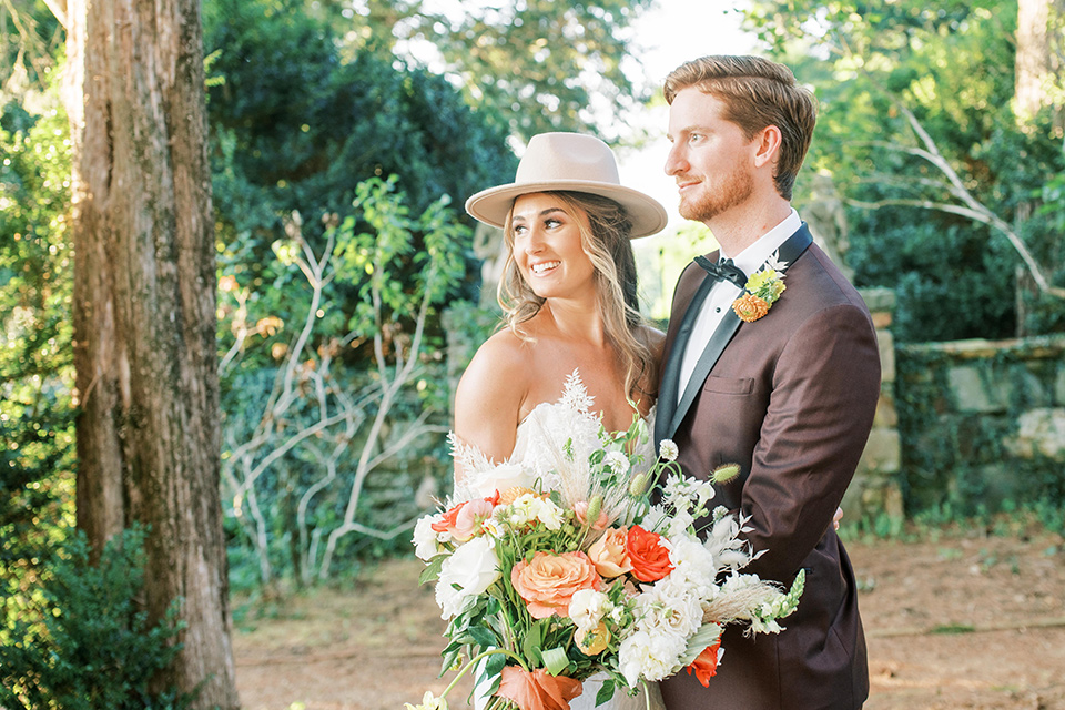  blush and burgundy wedding in the woods with the bride in a boho lace gown, the groom in a burgundy shawl tuxedo, and the bridesmaids in a dusty blush velvet gown – couple laughing