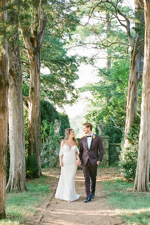  blush and burgundy wedding in the woods with the bride in a boho lace gown, the groom in a burgundy shawl tuxedo, and the bridesmaids in a dusty blush velvet gown – walking in the woods
