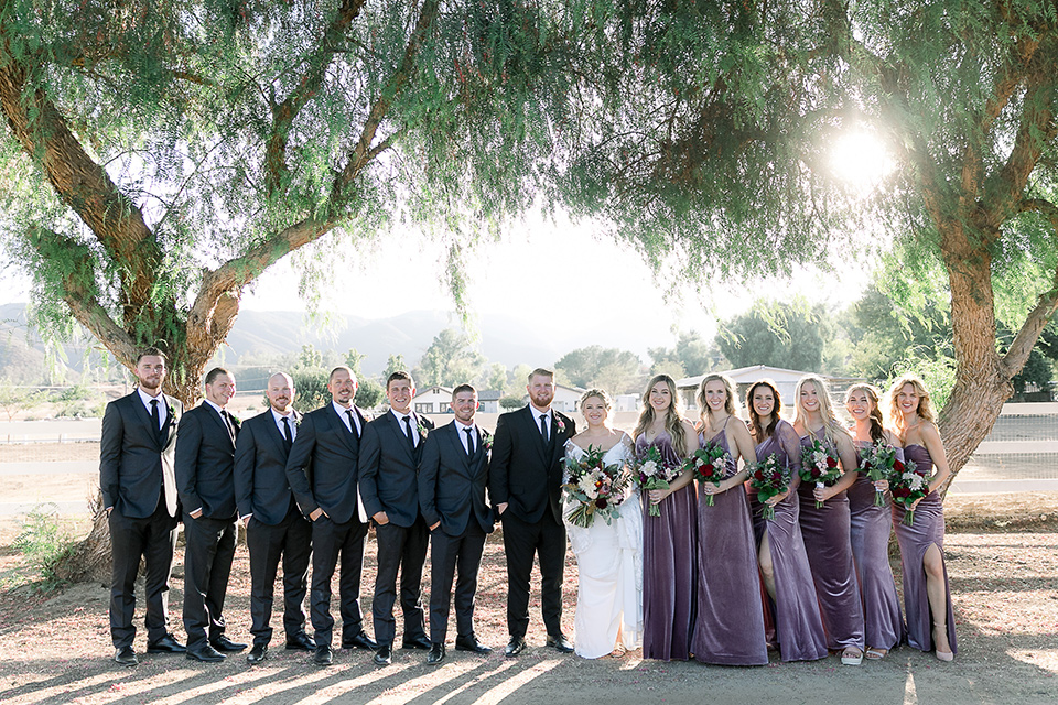  a lavender and black wedding in a garden – with the bride in a long sleeve lace gown and the groom in a black tuxedo – bridal party 