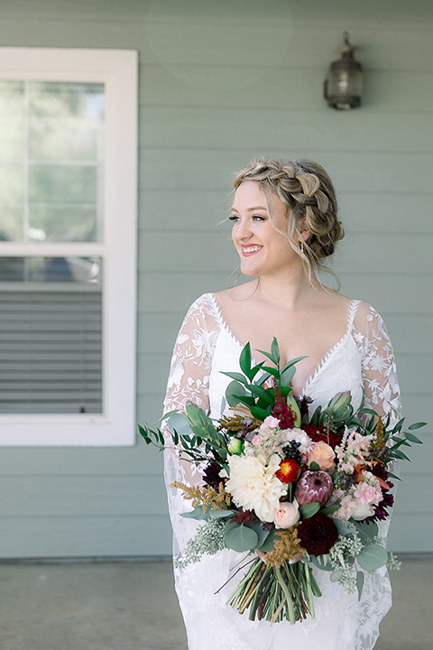  a lavender and black wedding in a garden – with the bride in a long sleeve lace gown and the groom in a black tuxedo – bride holding her flowers 