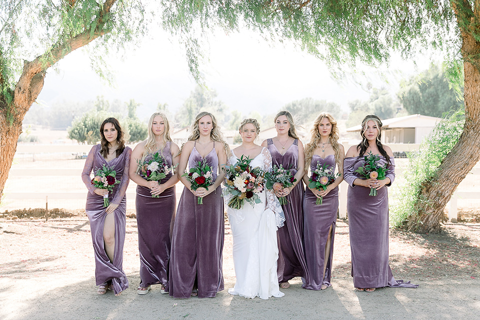  a lavender and black wedding in a garden – with the bride in a long sleeve lace gown and the groom in a black tuxedo – bridesmaids 