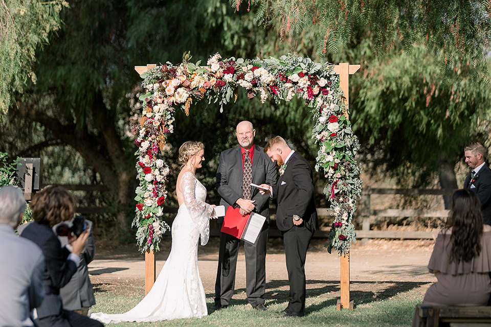  a lavender and black wedding in a garden – with the bride in a long sleeve lace gown and the groom in a black tuxedo – ceremony 