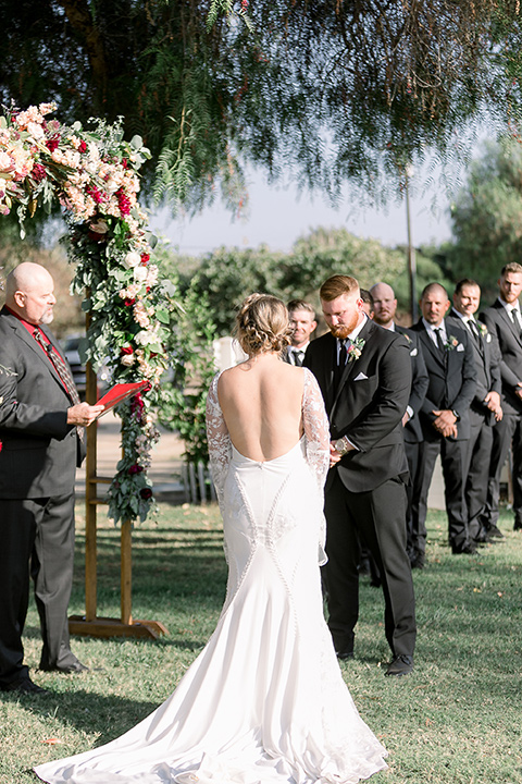  a lavender and black wedding in a garden – with the bride in a long sleeve lace gown and the groom in a black tuxedo – couple at the ceremony 