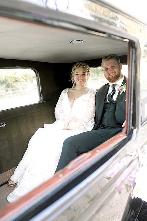  a lavender and black wedding in a garden – with the bride in a long sleeve lace gown and the groom in a black tuxedo – couple in the car 